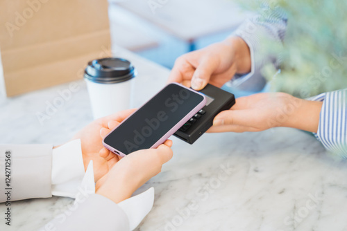 お店でコーヒーをスマートフォンのタッチ決済で購入する女性の手元 photo