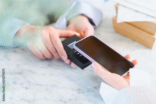 お店の商品をスマートフォンのキャッシュレス決済のタッチで買う女性の手元