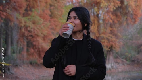 A young woman enjoys her coffee break in the park, holding a warm mug and savoring the comforting aroma.