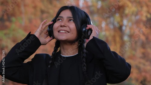  A cheerful woman with wireless earphones embraces the joy of music while relaxing outdoors.