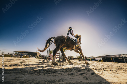 Spectaculaire contre-plongée d'un cavalier et de son cheval en plein mouvement sur un terrain de compétition équestre.