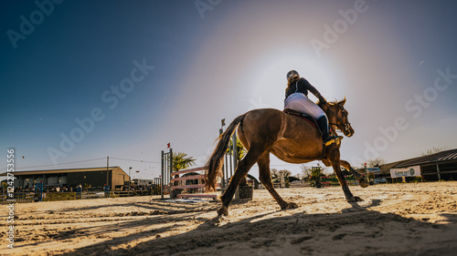 Spectaculaire contre-plongée d'un cavalier et de son cheval en plein mouvement sur un terrain de compétition équestre.