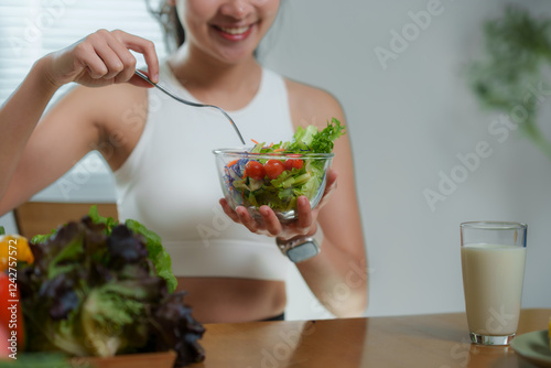 Smiling sportswoman enjoying a healthy vegetable salad filled with fresh tomatoes and crisp lettuce, seated at a table with a glass of milk, embracing a fitness-focused diet photo