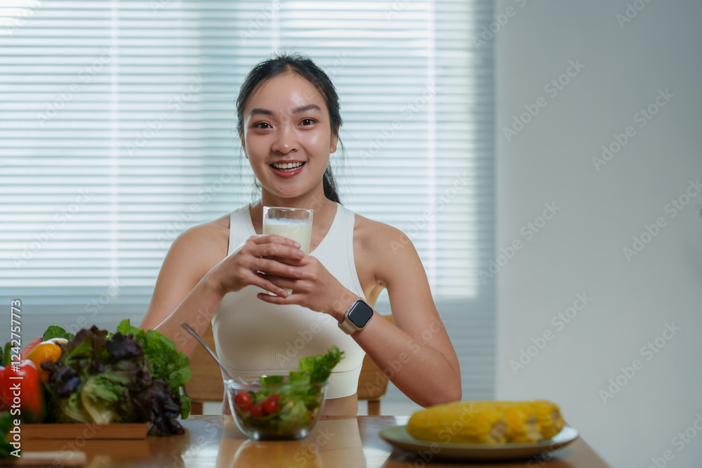 Young sporty asian woman drinking milk after workout, with healthy food such as vegetables and fruits on the table, promoting healthy lifestyle and balanced nutrition Young sporty asian woman drinking milk after workout, with healthy food such as vegetables and fruits on the table, promoting healthy lifestyle and balanced nutrition