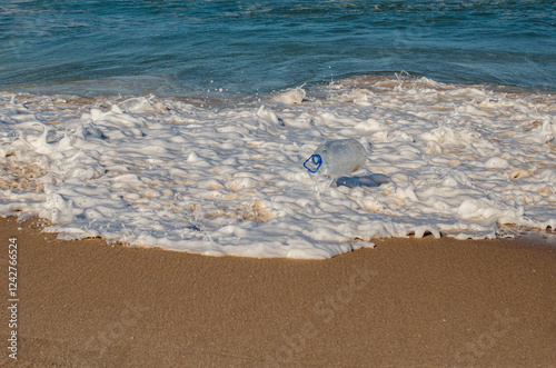 Wave washing up a plastic bottle on a tropical beach photo