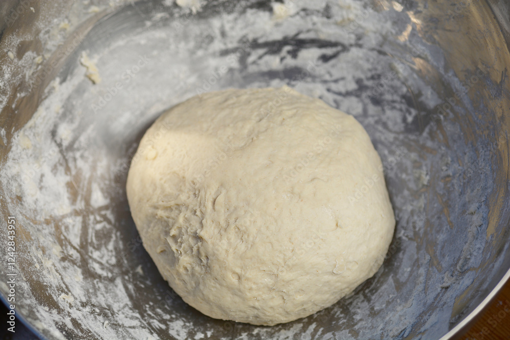 A round, raw dough sits in a metal bowl A round, raw dough sits in a metal bowl