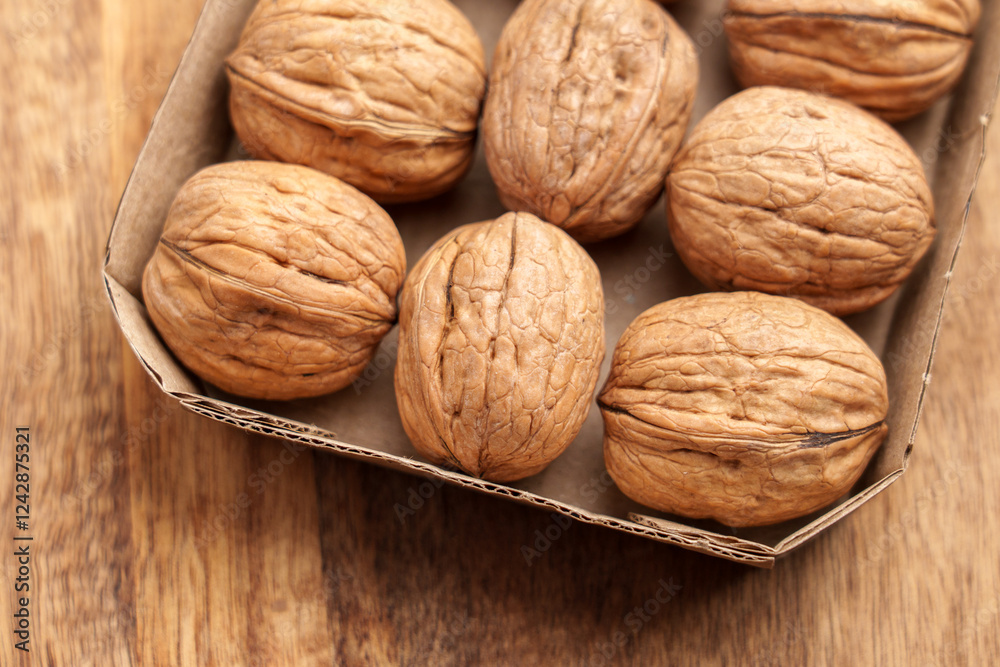 Organic walnuts in paper pack on wooden table. Unpeeled nuts with nutshell in cardboard box. Top view. Organic walnuts in paper pack on wooden table. Unpeeled nuts with nutshell in cardboard box. Top view.