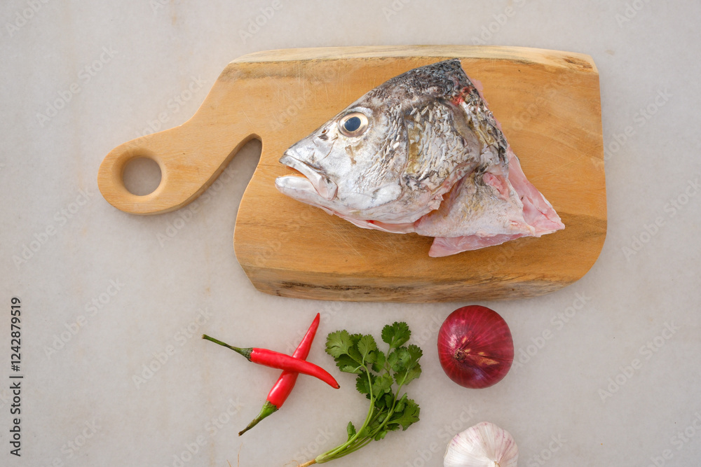 Raw golden snapper heads ready for cooking with some spices on wooden cutting board