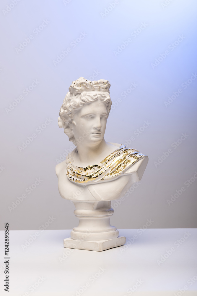 A classical white marble bust with intricate gold detailing on the draped garment, set against a gradient blue background. The sculpture's face is clearly visible, showcasing its detailed features. A classical white marble bust with intricate gold detailing on the draped garment, set against a gradient blue background. The sculpture's face is clearly visible, showcasing its detailed features.