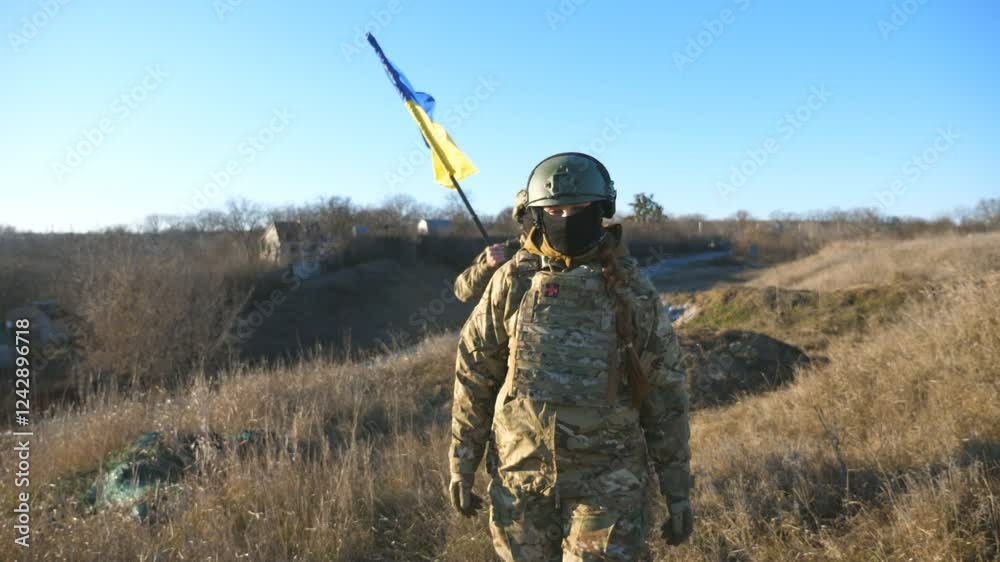 Young woman and man in military uniform going with national banner at meadow. Female and male soldier of ukrainian army walking with flag of Ukraine at field. Victory against russian aggression
