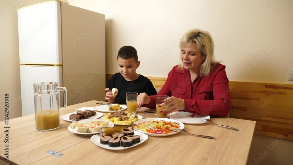 Mother and son sit at the festive table and enjoy delicious food. We celebrate at home. Mother and son sit at the festive table and enjoy delicious food. We celebrate at home.