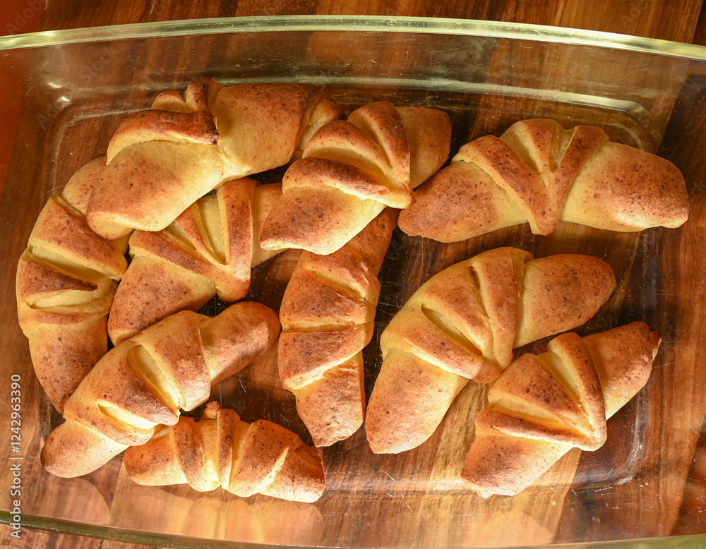 Freshly baked croissants cooling in a glass dish on a wooden countertop
