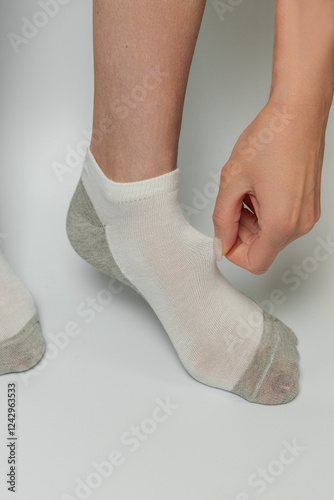 Close-up of woman putting on socks on her leg. White background