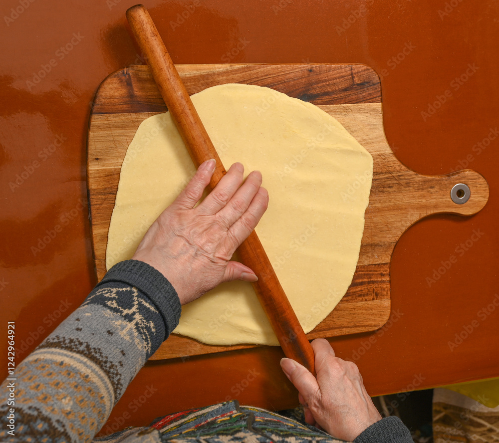 Elderly person rolling out dough on a wooden board in a cozy kitchen during a baking session