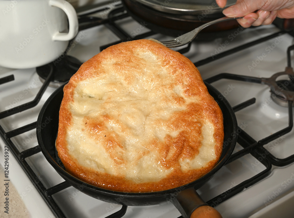 Freshly cooked flatbread being lifted from a skillet on a stovetop in a home kitchen