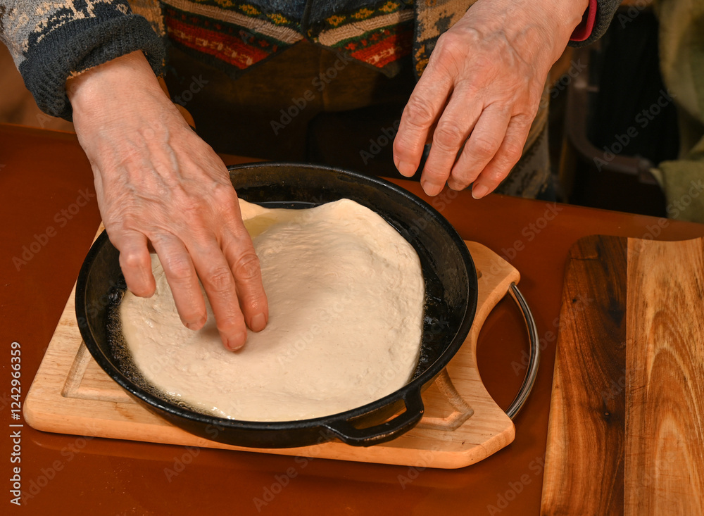 Hands shaping dough on a cast iron skillet during cooking preparation in a cozy kitchen