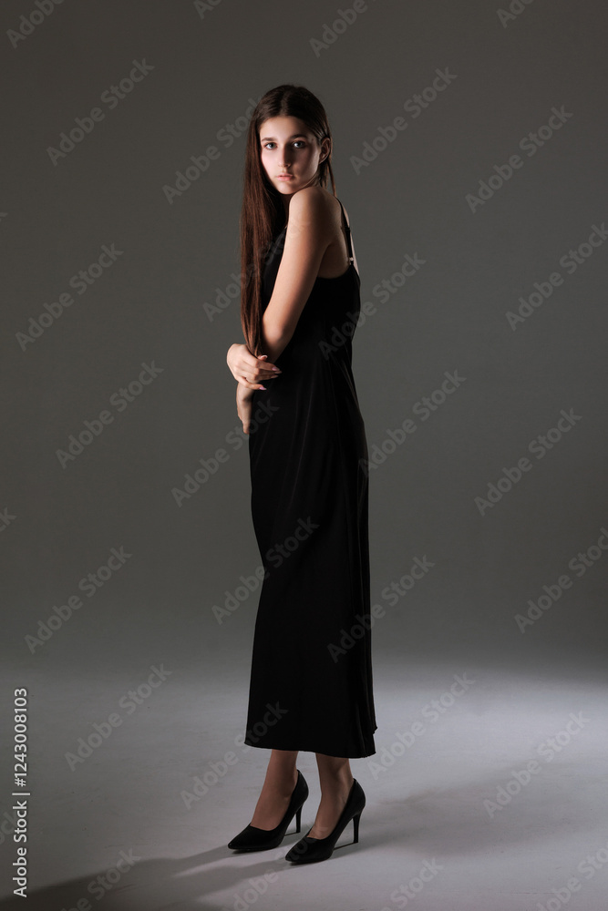Model poses elegantly in a black gown with high heels against a studio backdrop Model poses elegantly in a black gown with high heels against a studio backdrop