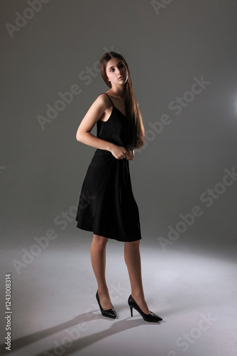 Elegant young woman poses gracefully in a sleek black dress against a neutral background