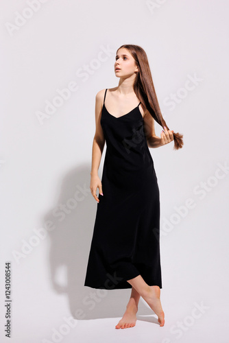 Model poses in a black dress showcasing a delicate and elegant look with long hair on a simple background