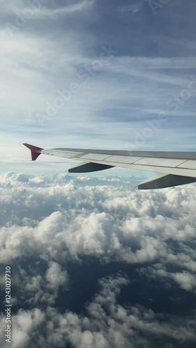 View from the airplane window to the clouds, the plane flies over the sea. Vertically footage.