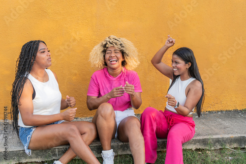 Three latin american women laughing together in front of yellow wall