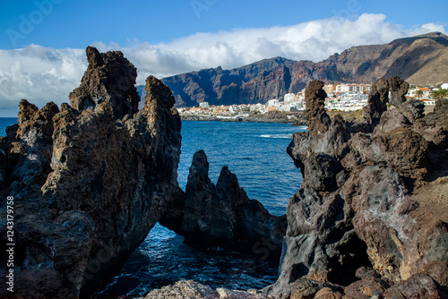 Charco La Vaca in Tenerife, Spain. Charcos Los Turistas park with lava rock formations and cave in the ocean. Los Gigantes seen in the distance. photo