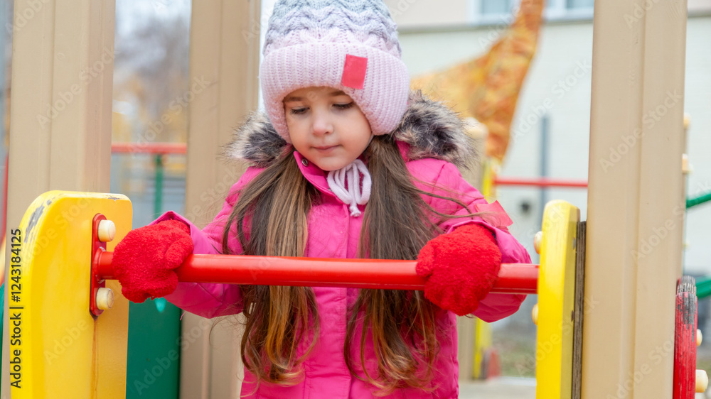 Little girl having fun on playground. Happy healthy little child climbing, swinging and sliding on different equipment. Child on cold day in colorful clothes outdoors Little girl having fun on playground. Happy healthy little child climbing, swinging and sliding on different equipment. Child on cold day in colorful clothes outdoors
