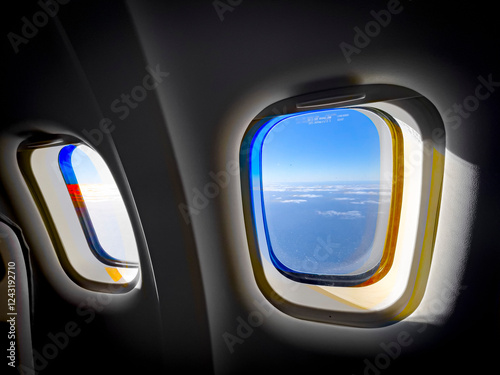 Scenic view through two airplane windows showing the ocean, blue sky, and clouds. Sunlight reflections create a colorful effect, enhancing the sense of travel and altitude. photo