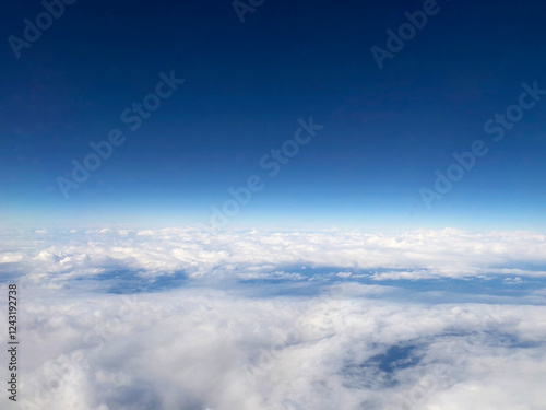 Expansive aerial view of white clouds stretching to the horizon under a deep blue sky. The high-altitude perspective captures the beauty of air travel and nature. photo