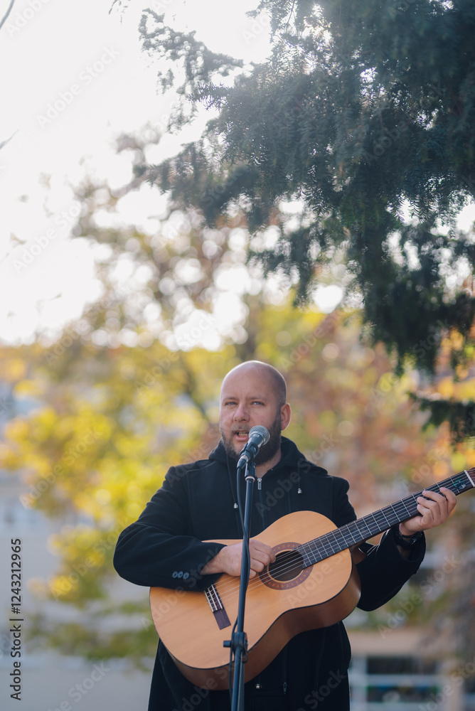 Fototapeta premium Musician singing and playing acoustic guitar outdoors in autumn