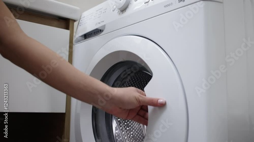 A woman's hand takes freshly washed clothes from the washing machine in the bathroom. Concept: dry cleaning and cleaning services that simplify clothing care and maintain order at home.