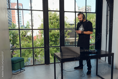 Young arabic Man using phone while making music with his dj mixer panel.