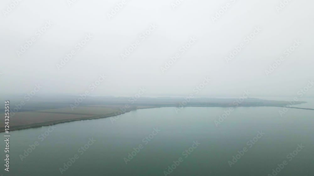 Droning over a serene lakeside landscape with misty mountains in the distance Droning over a serene lakeside landscape with misty mountains in the distance