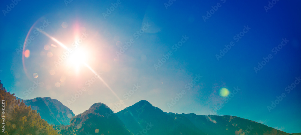 Silhouette of mountains against a clear blue sky with sun. Horizontal banner