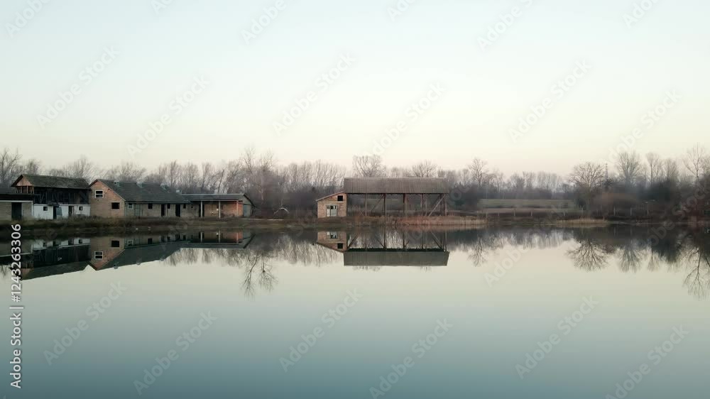 Calm sunset reflection on a serene lake with rustic buildings along the shore in a tranquil countryside setting Calm sunset reflection on a serene lake with rustic buildings along the shore in a tranquil countryside setting