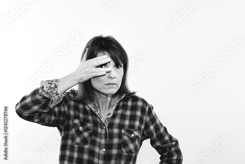 Schwarz-Weiß-Porträt einer Frau mit langen Haaren in einem karierten Hemd, das Gesicht teilweise mit der Hand verdeckt und den Blick durch die gespreizten Finger gerichtet photo