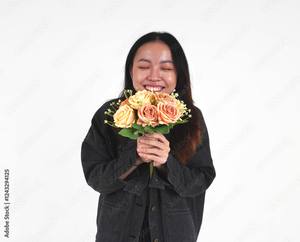 Happy asian young woman with long hair wearing denim jacket and black pants sniffing rose flowers isolated on horizontal white background. Happy asian young woman with long hair wearing denim jacket and black pants sniffing rose flowers isolated on horizontal white background.