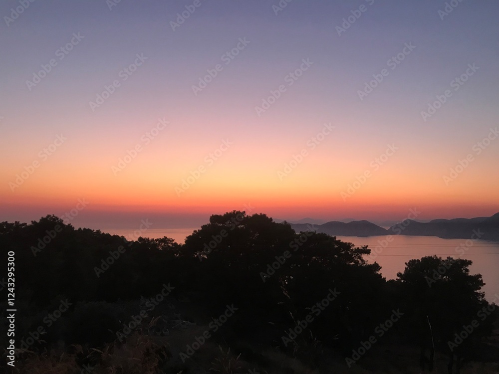 Obraz premium A vibrantly coloured sky during sunset over the mountains and sea 