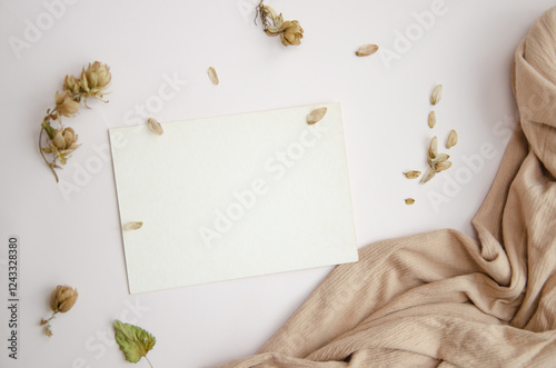 Blank paper card on white background with dried plants and wavy beige fabric, top view. Boho mock-up scene with greeting card template photo