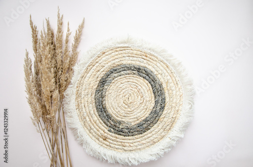 A round woven placemat, and dry spikelets on a light beige background.dry spikelets. Mock up. Concept of home comfort and interior elements.