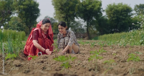 Indian active mother wear saree teen age cute girl sitting help and protect to grow tree in red soil young adult farmer female woman with lady talk gossip do nature care enjoy day desi life garden