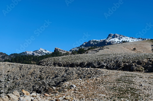 Rocky landscape with snow-capped mountains under a bright blue sky. photo