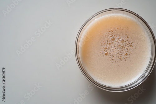 A single petri dish filled with ultrafine beige powder is centered on a white laboratory countertop, displaying soft shadows that enhance the minimalist aesthetic photo