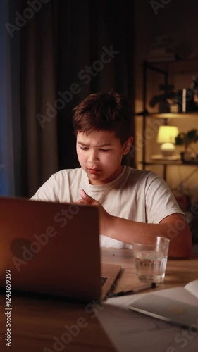 Teen boy sitting at desk stretching neck and feeling pain after long screen time or online studying at home Child with beck discomfort after hours of remote learning