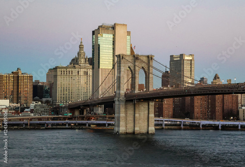 Brooklyn Bridge and New York skyline at sunrise, Brooklyn, NY, USA. Sun reflecting on the bridge and the office buildings behind as daylight shines across the East River.