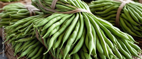 Bundles of fresh petai beans with long flat green pods tied together ready for sale in a market setting showcasing their vibrant freshness. photo