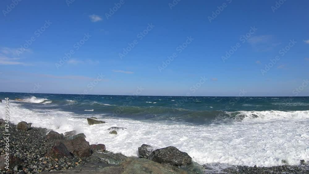 A scenic view of a rocky beach with waves crashing against the shoreline. The deep blue sea stretches to the horizon under a clear sky with a few wispy clouds. The foamy white surf contrasts with the A scenic view of a rocky beach with waves crashing against the shoreline. The deep blue sea stretches to the horizon under a clear sky with a few wispy clouds. The foamy white surf contrasts with the
