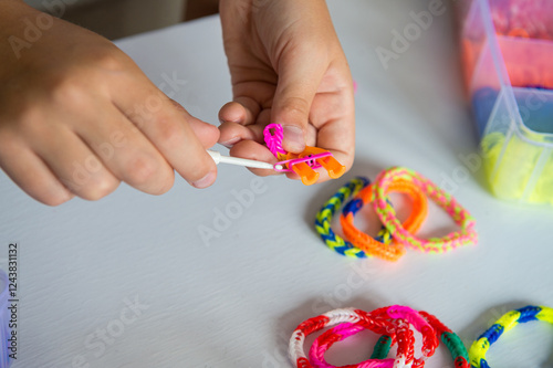 Child crafting colorful loom bands with hook on white table photo