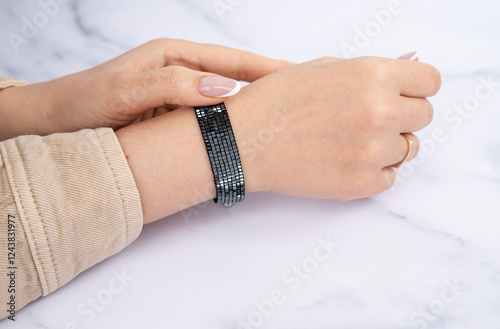 Caucasian female hand displaying black beaded bracelet on marble surface. National Accessory Day photo