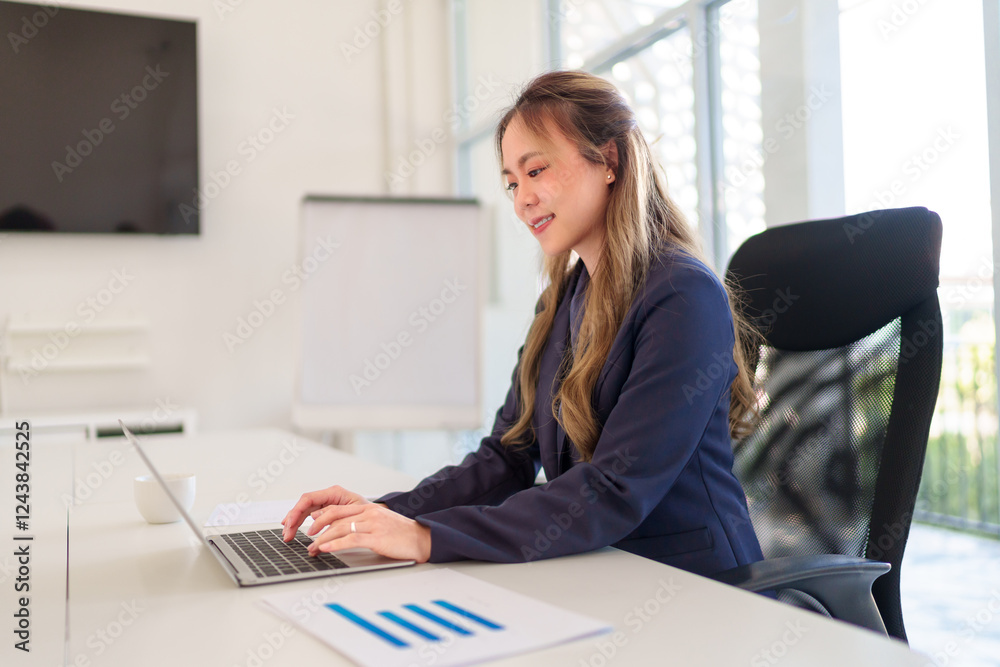 Young Asian businesswoman taking notes while working on a laptop at her office desk in a modern workspace Young Asian businesswoman taking notes while working on a laptop at her office desk in a modern workspace